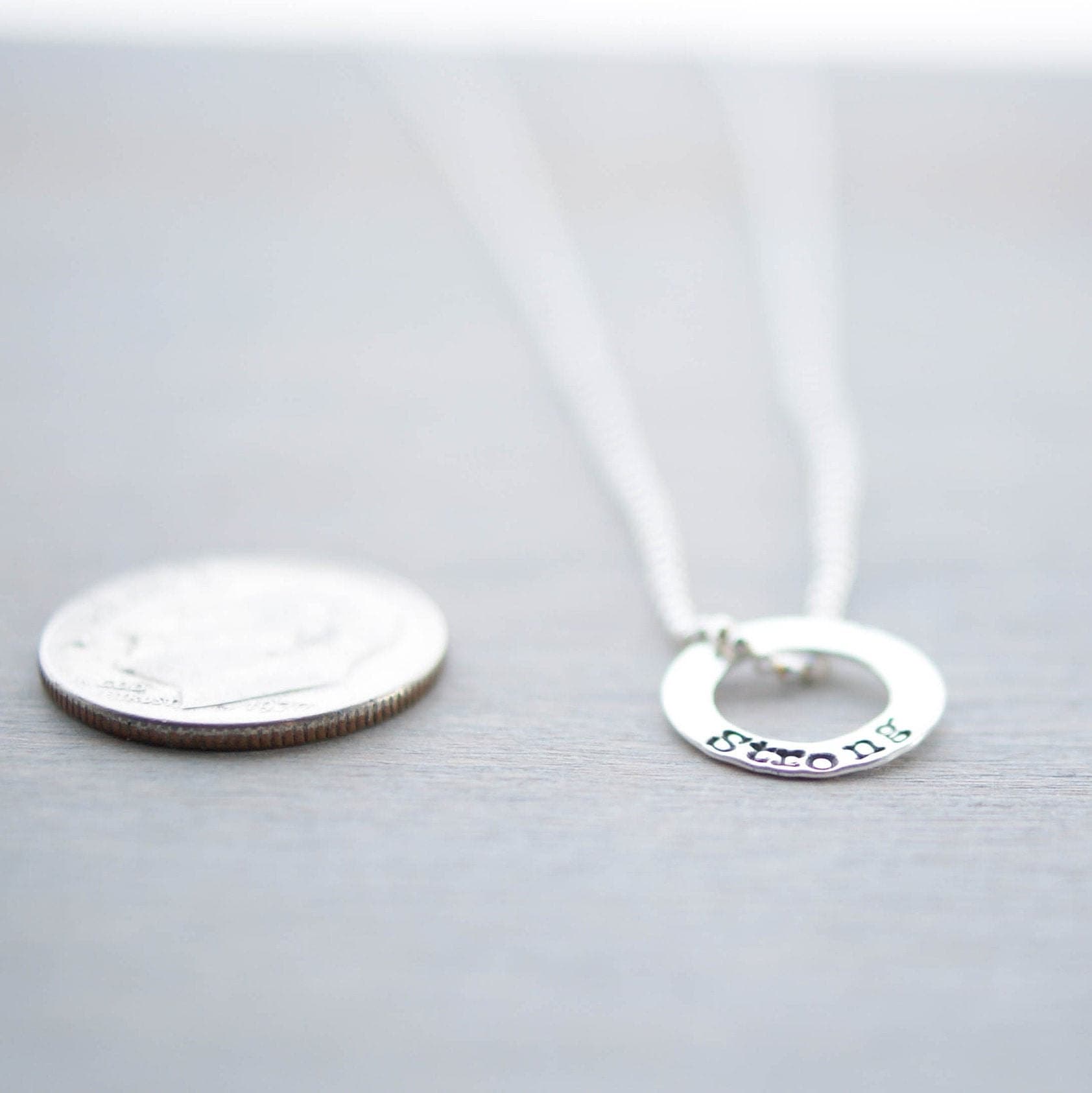 Sterling silver tiny circle stamped with Strong necklace next to dime