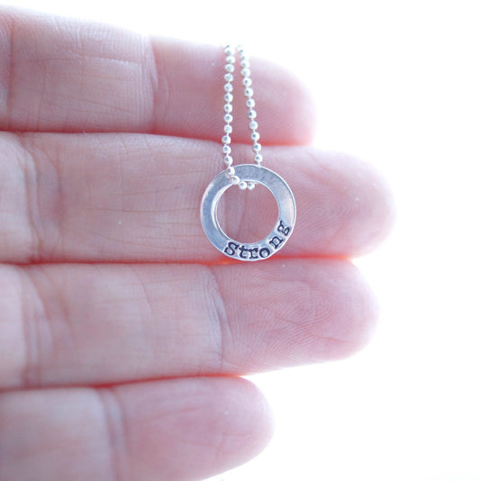 Sterling silver tiny circle stamped with Strong necklace in hand