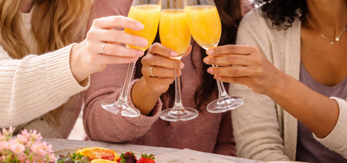 image of 3 girls toasting mimosas up close on the glasses for Galentine's Day