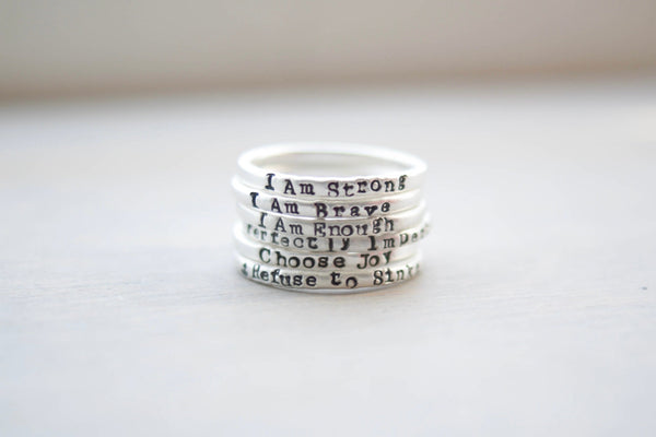 image of a stack of sterling silver affirmation  rings on a grey background