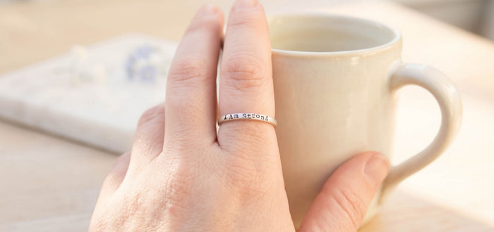 Sterling silver I Am Strong ring representing strength, resilience, and self-trust on hand holding mug.