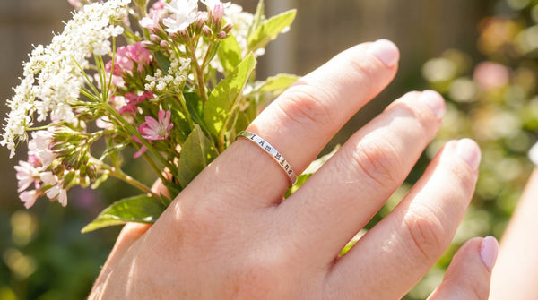 hand wearing sterling silver I Am Mine ring on index finger while holding wildflowers