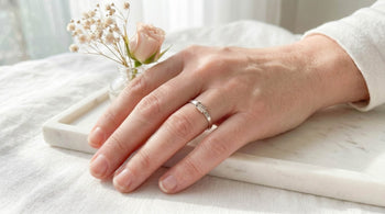 image of hand wearing a sterling silver fidget ring  with white background and flower behind