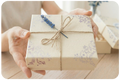 Gift box with floral wrapping and string held by hands on a wooden surface