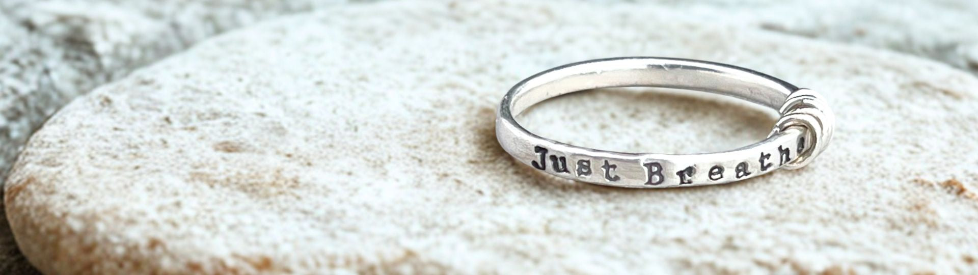 Silver ring with 'Just Breathe' engraving on a textured stone surface