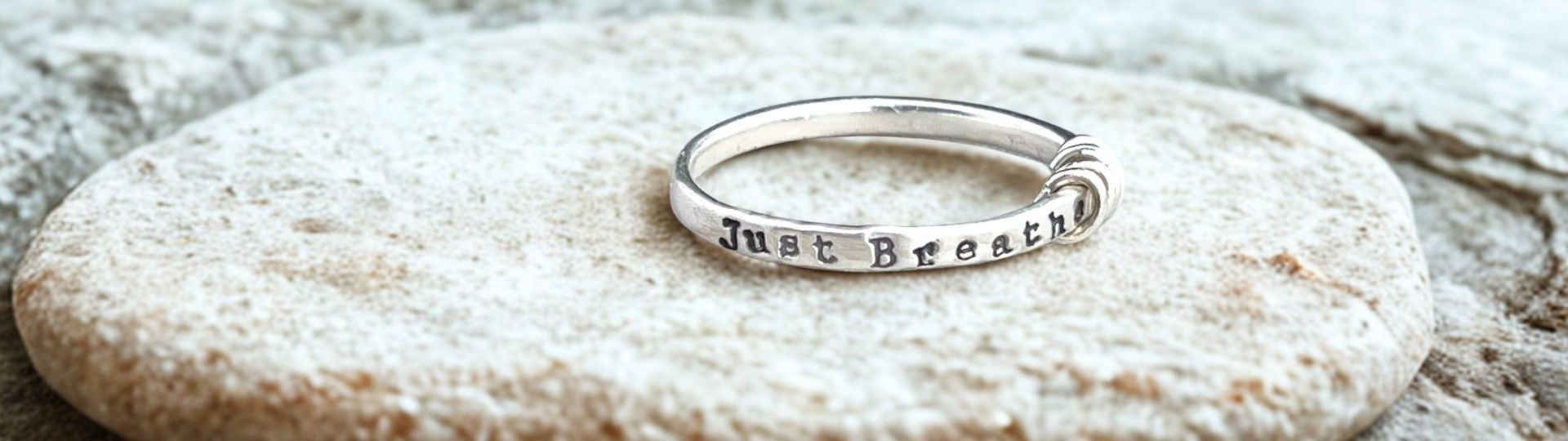 Silver ring with 'Just Breathe' engraving on a textured stone surface