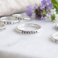 Custom Personalized choose your word ring in sterling silver stamped with Breathe on a white background with flowers and other rings behind.