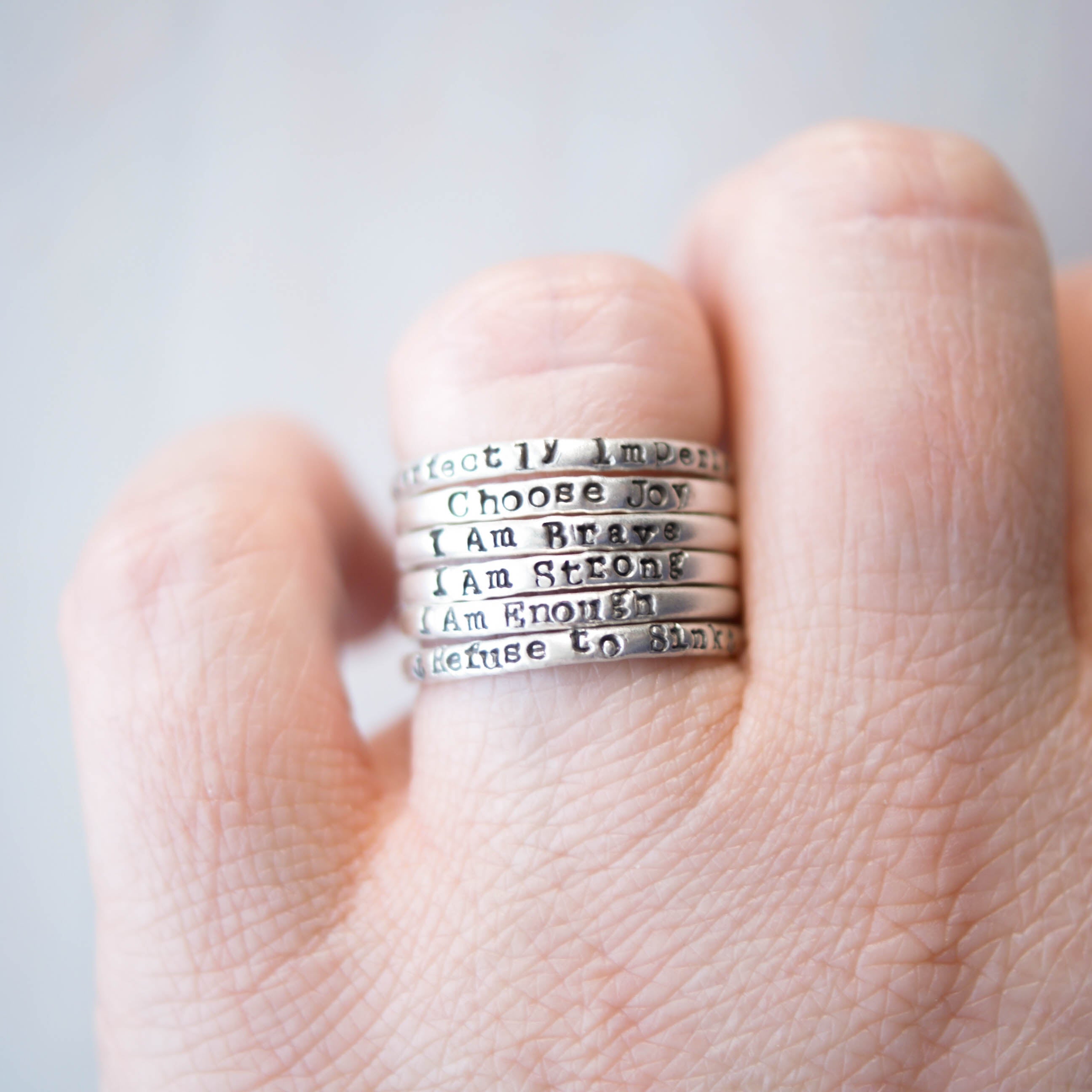 Stack of silver rings with motivational phrases on a hand against a light background