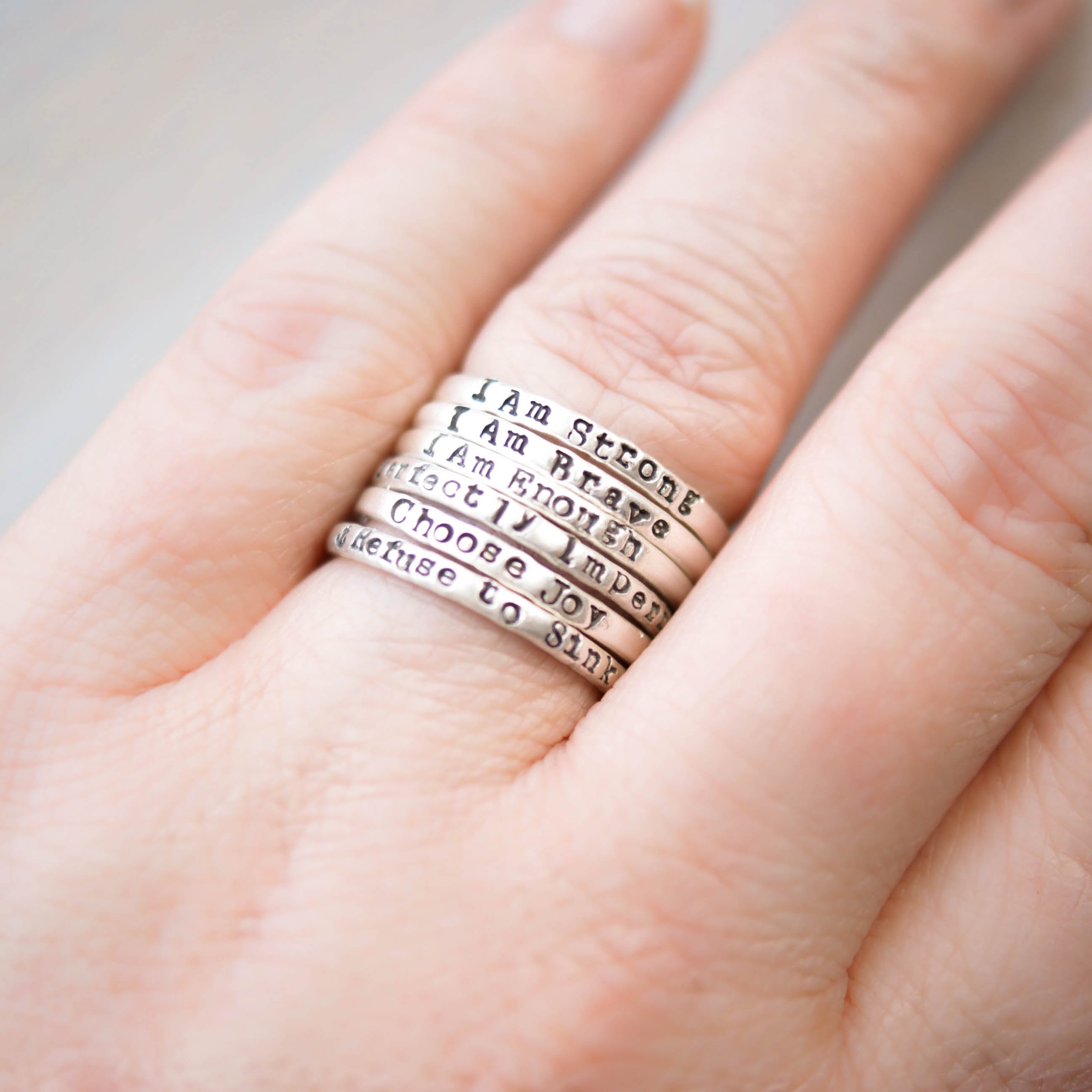 Stack of silver motivational rings on a hand against a neutral background