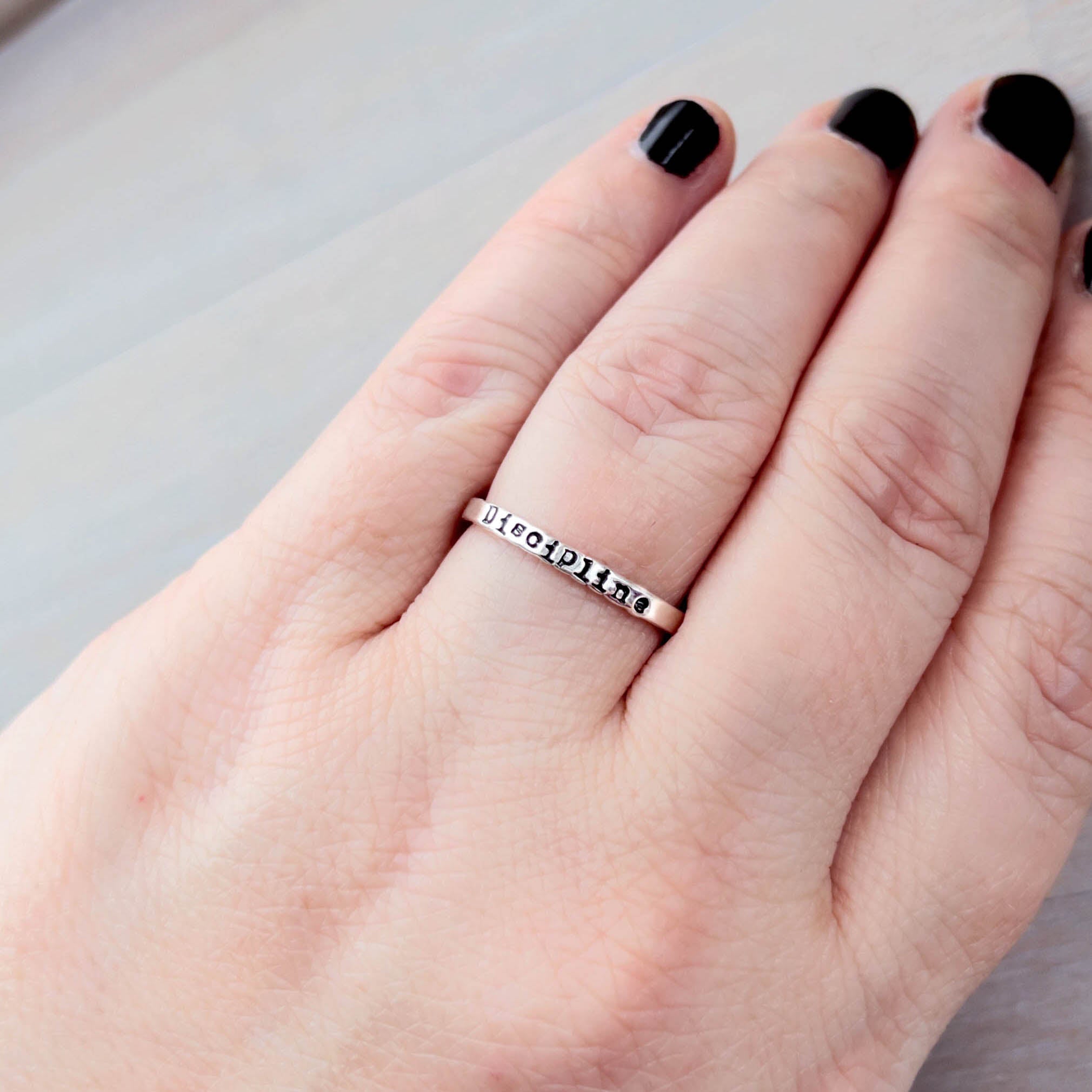 Hand wearing a silver ring with Discipline on it on a neutral background