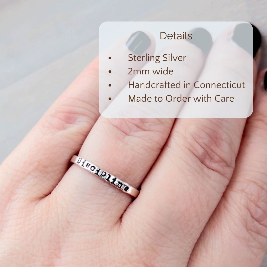 Image of Custom Word of the Year ring stamped on a hand with the product details overlayed. Sterling silver, 2mm wide, handcrafted in connecticut, made to order with care.