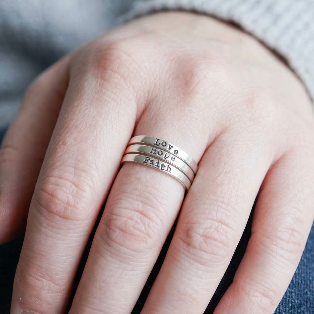 Three sterling silver rings with Faith Hope and Love on them on a person's finger
