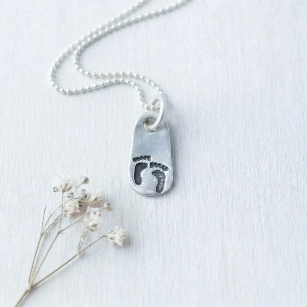 Silver artisan pewter necklace with a footprints pendant on a light background
