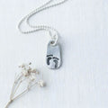 image of silver pendant with little baby footprints on a grey background with small flower below