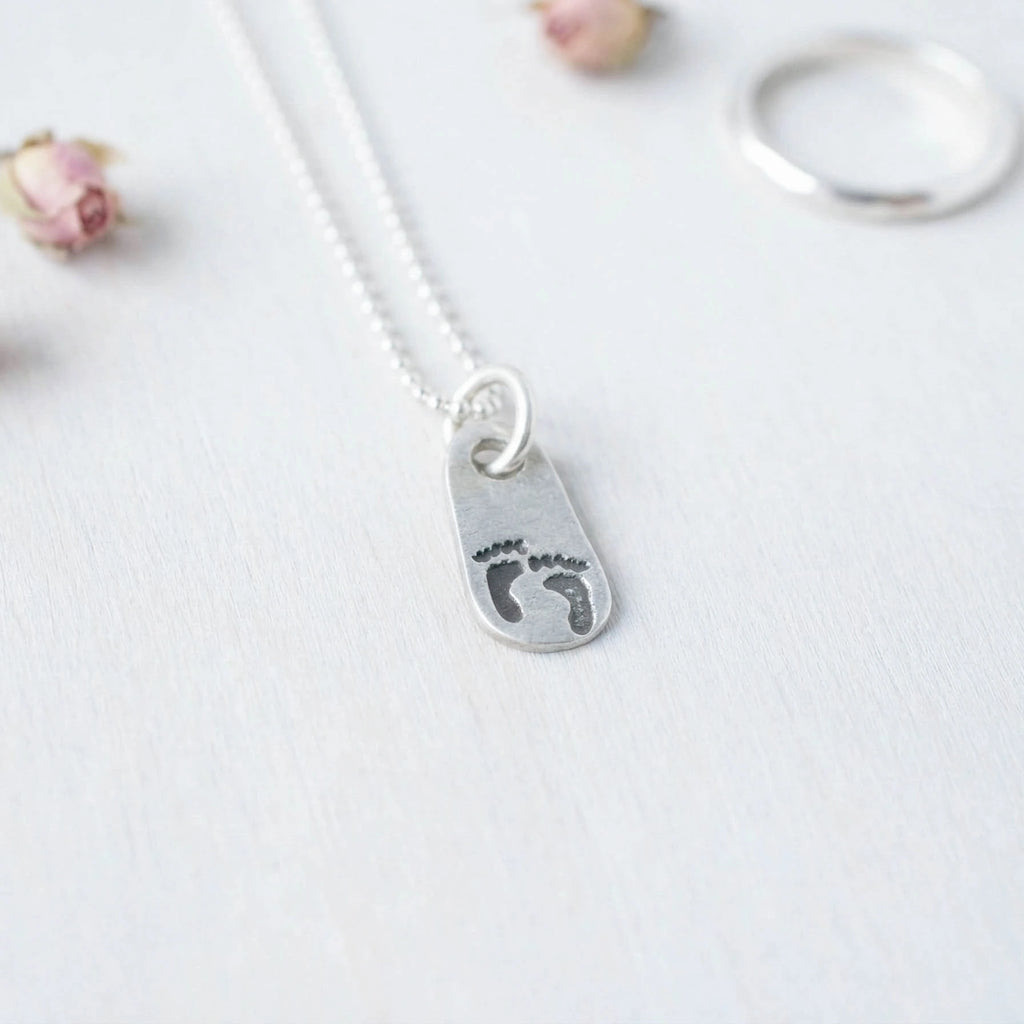 Silver necklace with a pendant featuring footprints on a light gray background
