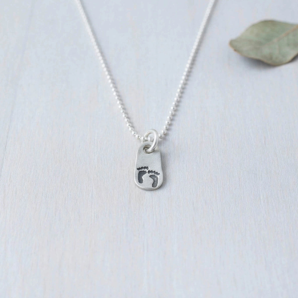Silver necklace with a footprints pendant on a light background