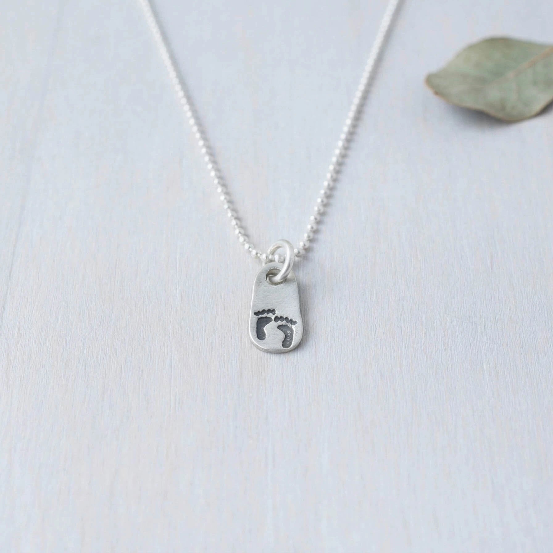 Silver necklace with a footprints pendant on a light background