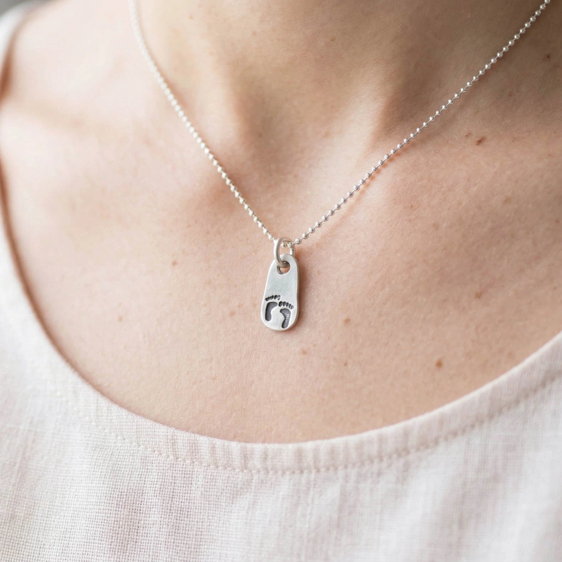 Silver necklace with a baby feet charm worn by a woman