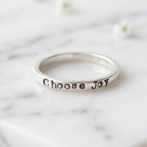Silver ring with 'Choose Joy' stamped on a marble surface