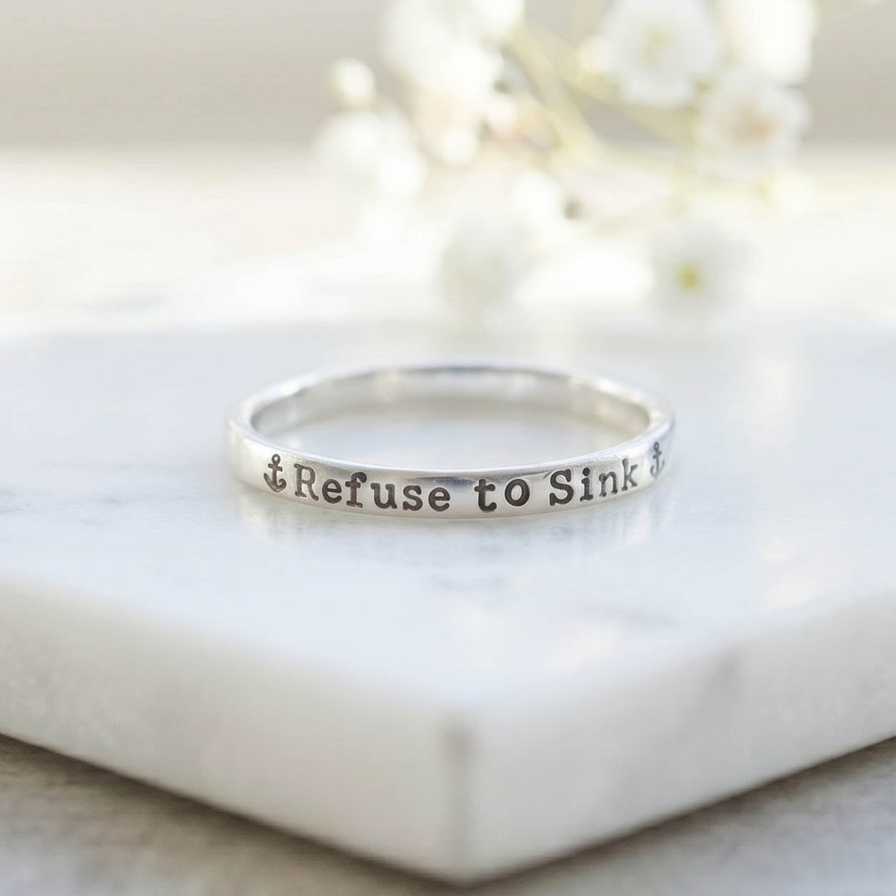 Silver ring with 'Refuse to Sink' stamped on a marble surface