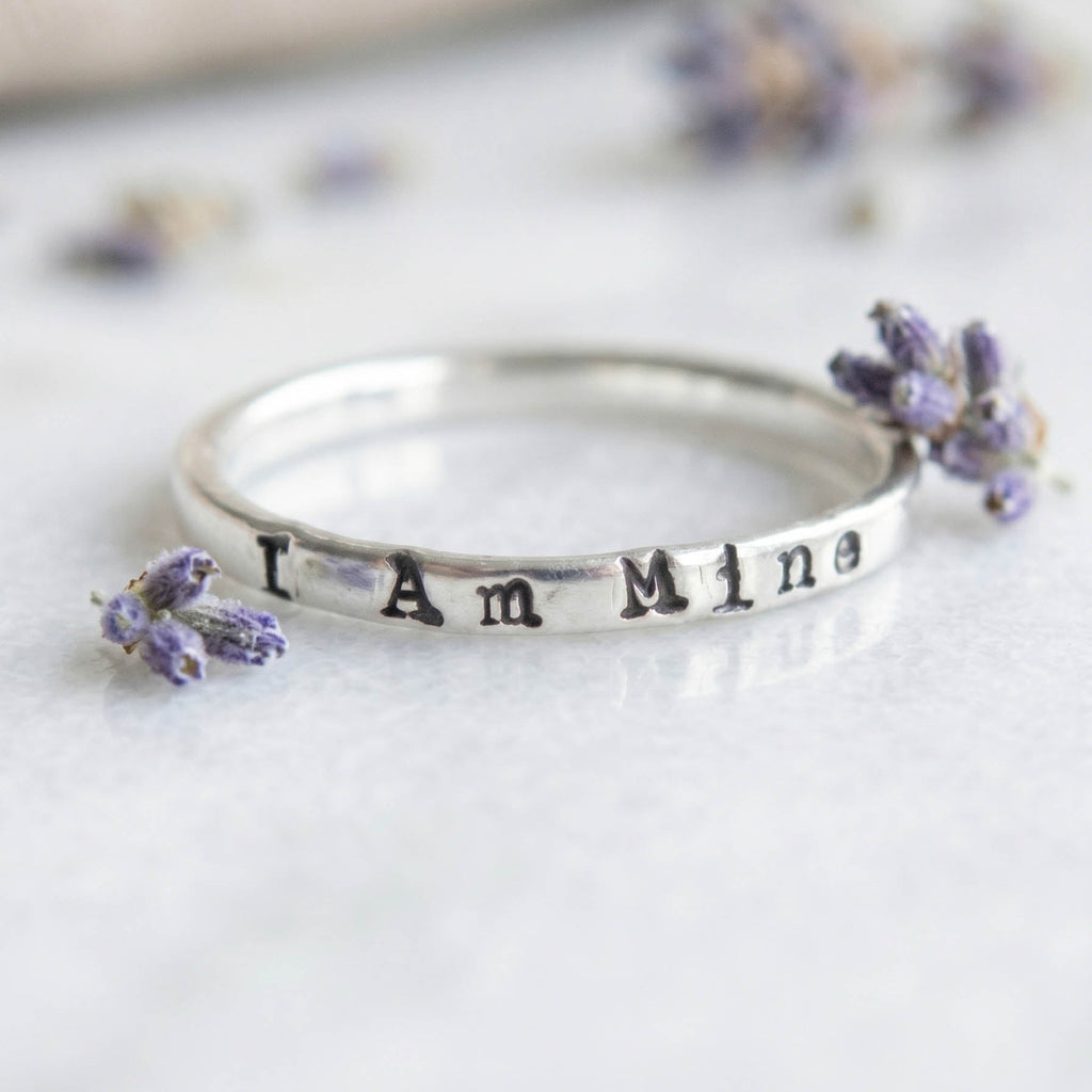 Silver ring with 'I Am Mine' stamped on a white background with lavender flowers.