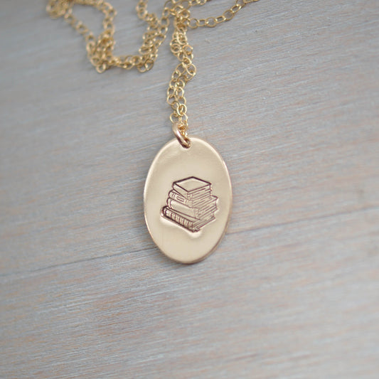 Gold oval necklace stamped with a stack of books