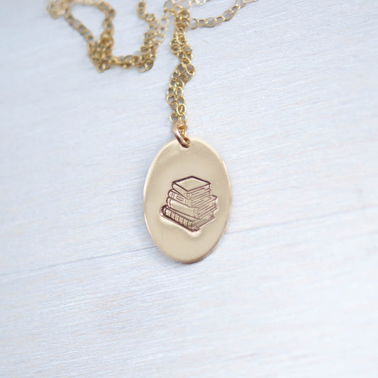 Gold oval necklace stamped with a stack of books