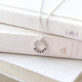 A silver necklace with a circular pendant engraved with the word 'Bookish' in black lettering, draped over stacked cream-colored books.