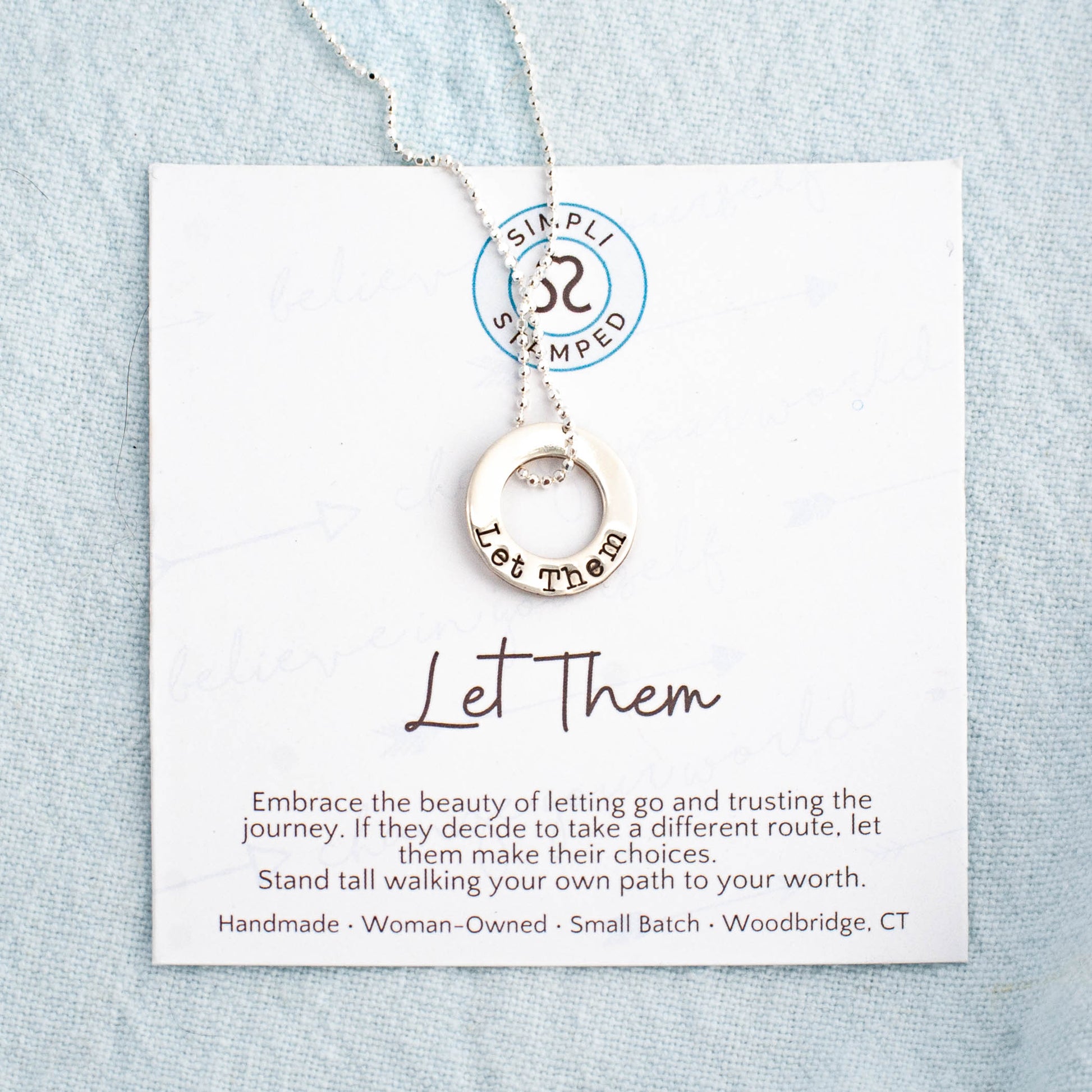 image of sterling silver washer necklace stamped with "let them" on a motivational card