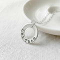 Silver washer necklace with Let Them stamped on it on a white surface