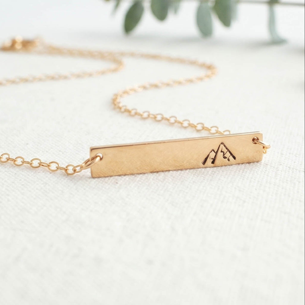 Gold You will move mountains necklace with a bar pendant on a light background