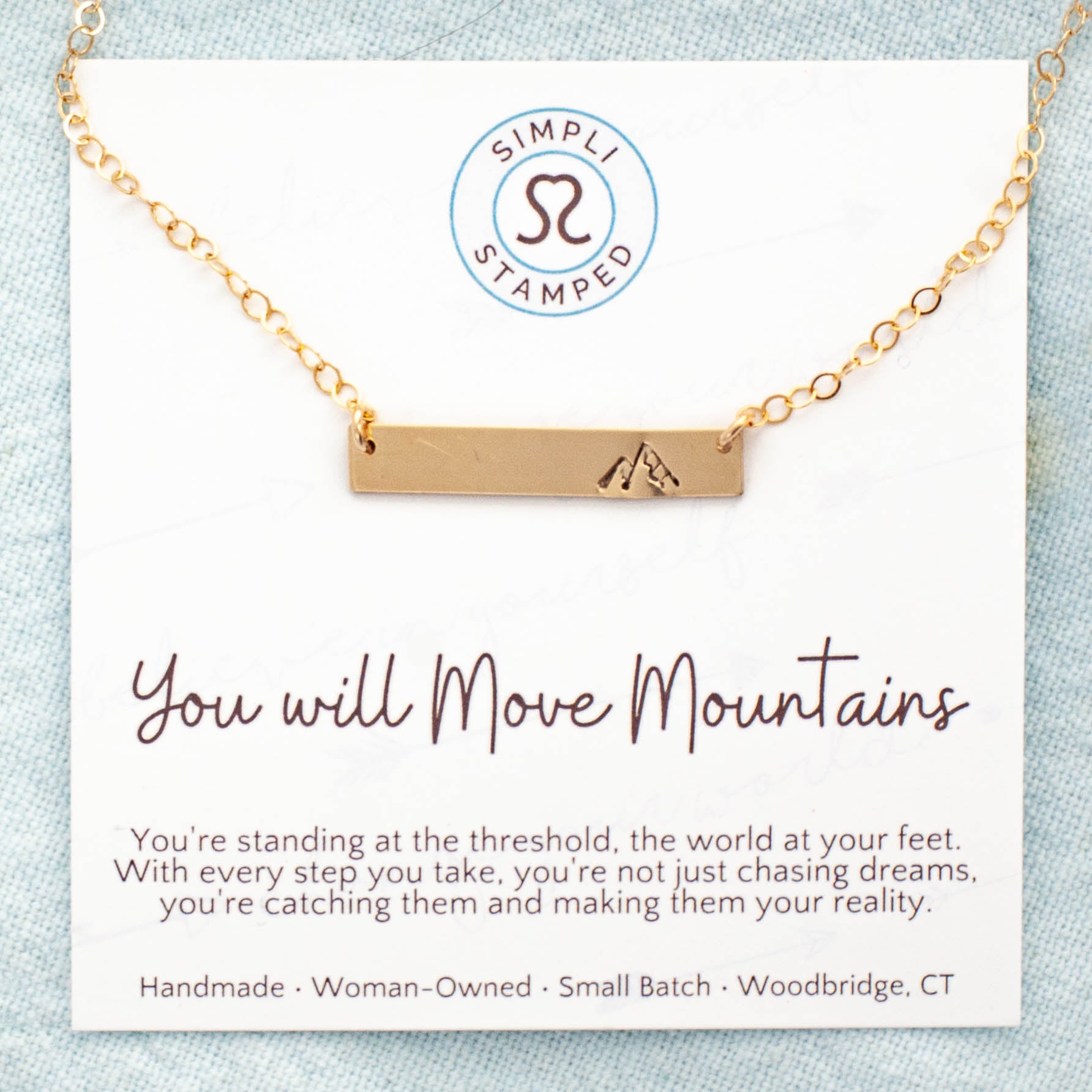 mage of gold necklace with mountain stamped on the right side on card with motivational card.