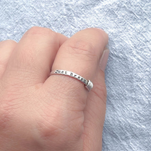 image of sterling silver ring stamped with Just Breathe on a hand