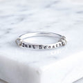 A sterling silver fidget ring with the words 'Just Breathe' hand-stamped on the front, resting on a white marble surface.