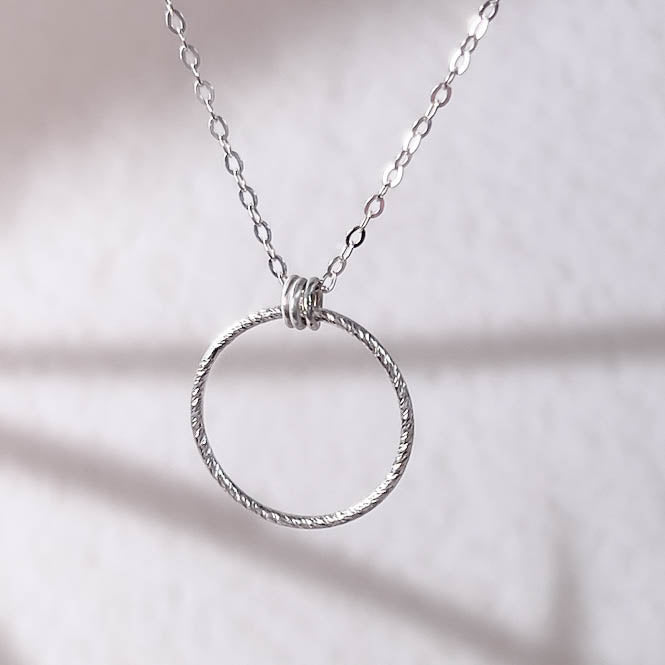 Silver circular pendant necklace on a soft pink background