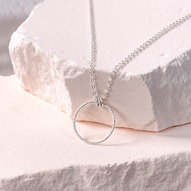 Silver necklace with a circular pendant on a light stone surface