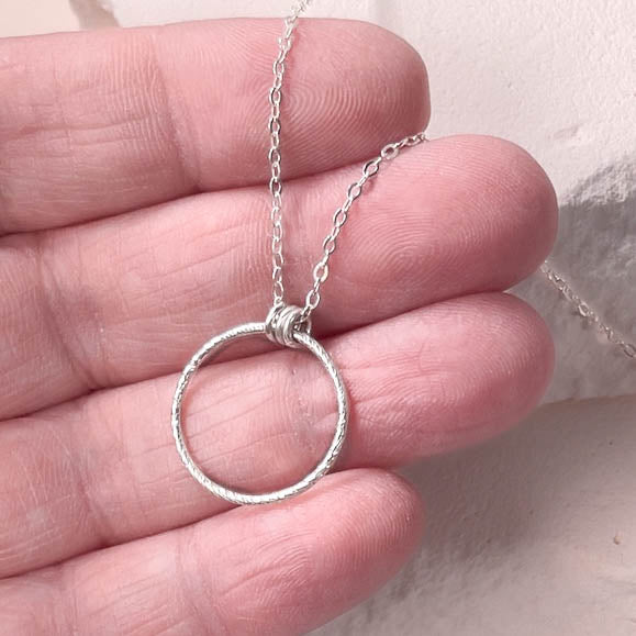 Silver circle pendant necklace held in a hand against a neutral background