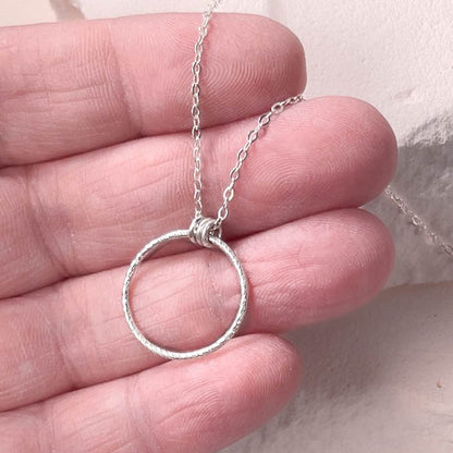 Silver circle pendant necklace held in a hand against a neutral background