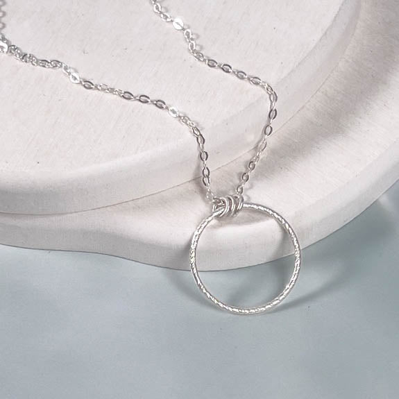 Silver necklace with a circular pendant on a light gray background
