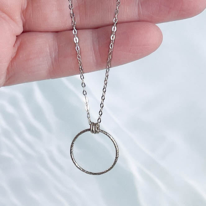 Silver necklace with a circular pendant held by a hand on a light background