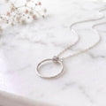 sterling silver calm within fidget necklace on a marble surface with flowers behind