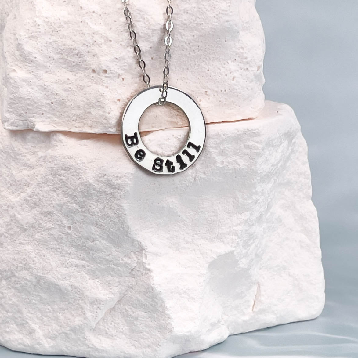 Silver necklace with a circular pendant on a white stone surface