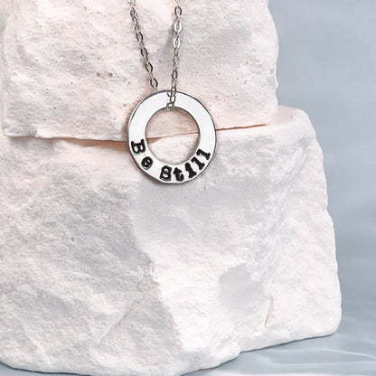 Silver necklace with a circular pendant on a white stone surface