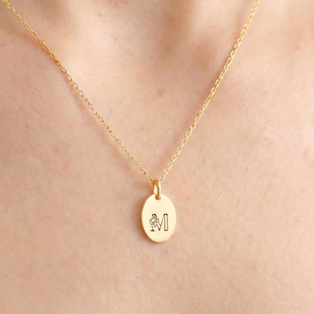 Gold necklace with a floral initial pendant on a person's neck