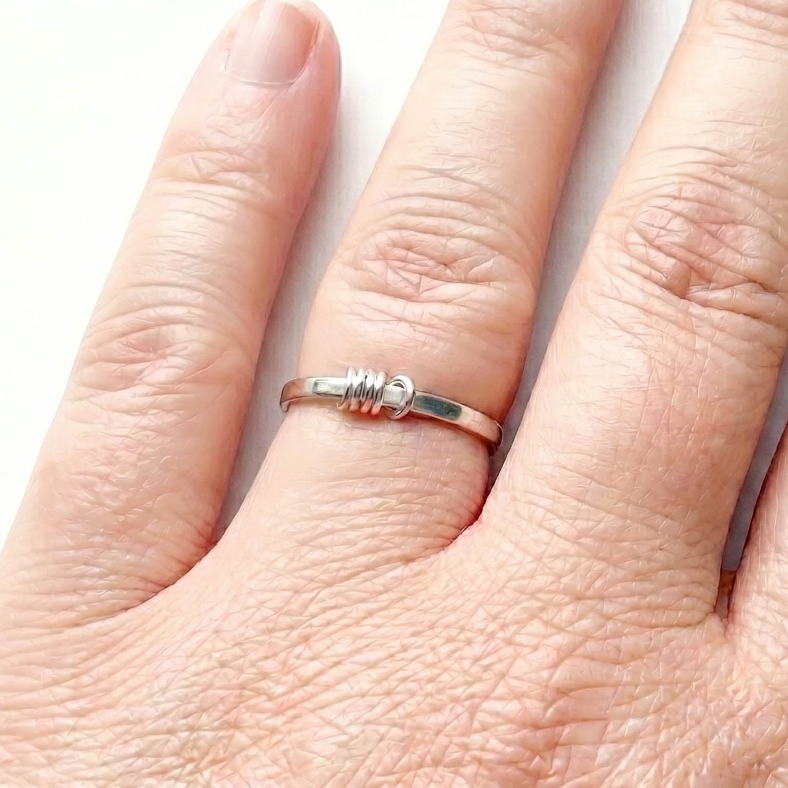 Close-up of a hand wearing a sterling Silver fidget ring with a 5 outside spinner rings on a light gray background