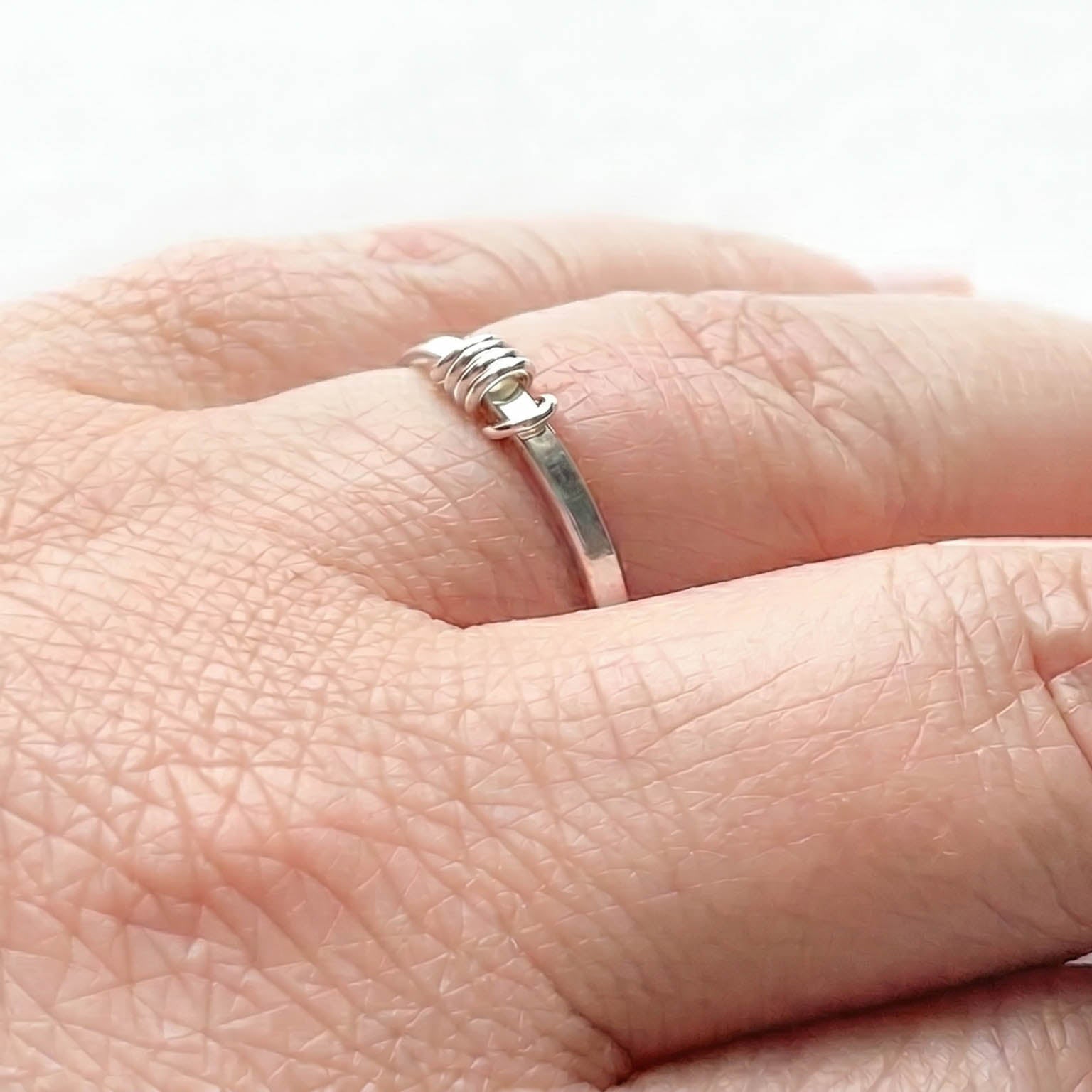 Close-up of a hand wearing a sterling Silver fidget ring with a 5 outside spinner rings on a light gray background