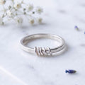 A silver spinner ring resting on a light marble surface with small white flowers and lavender buds in the background.