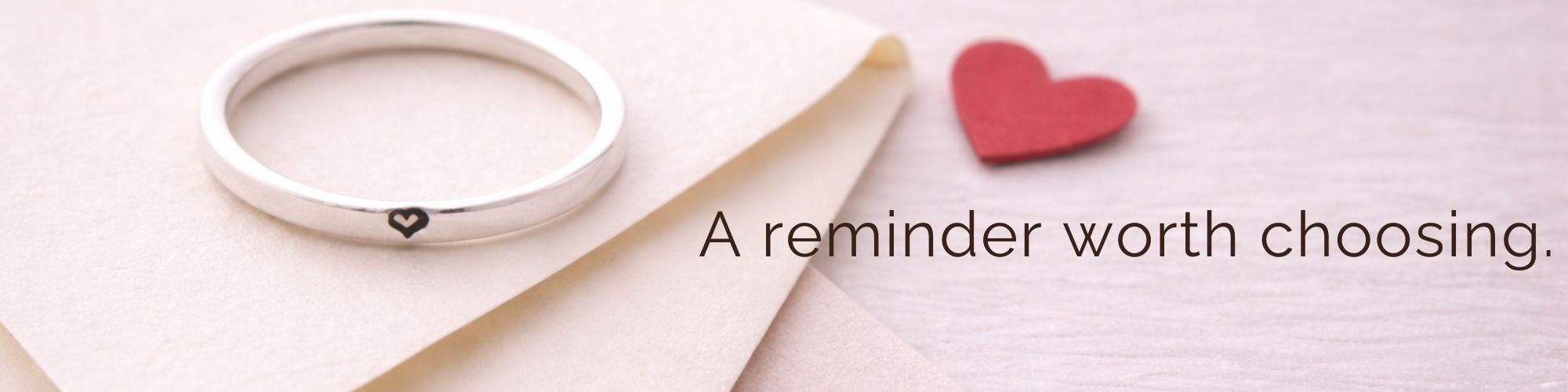 Silver ring with engraved heart on a white surface with a red heart, text 'A reminder worth choosing'.