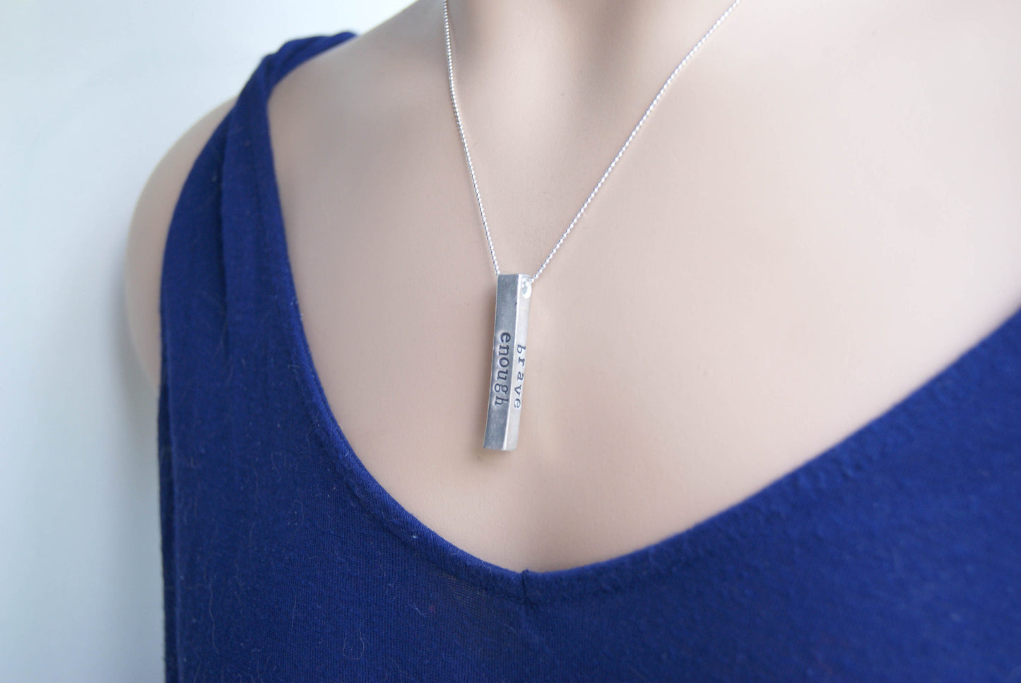 Long bar necklace stamped with strong, brave, and enough in artisan pewter on neck