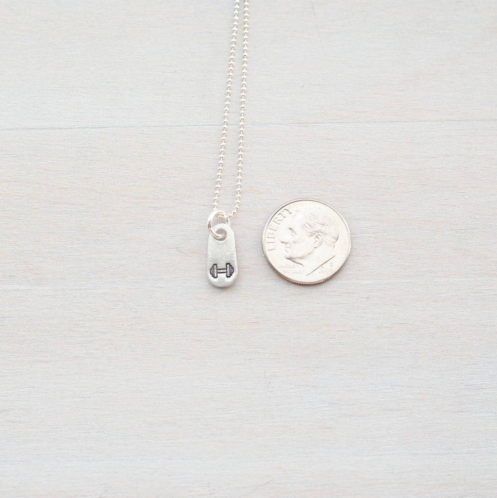Silver fitness jewelry dumbbell necklace in artisan pewter next to dime